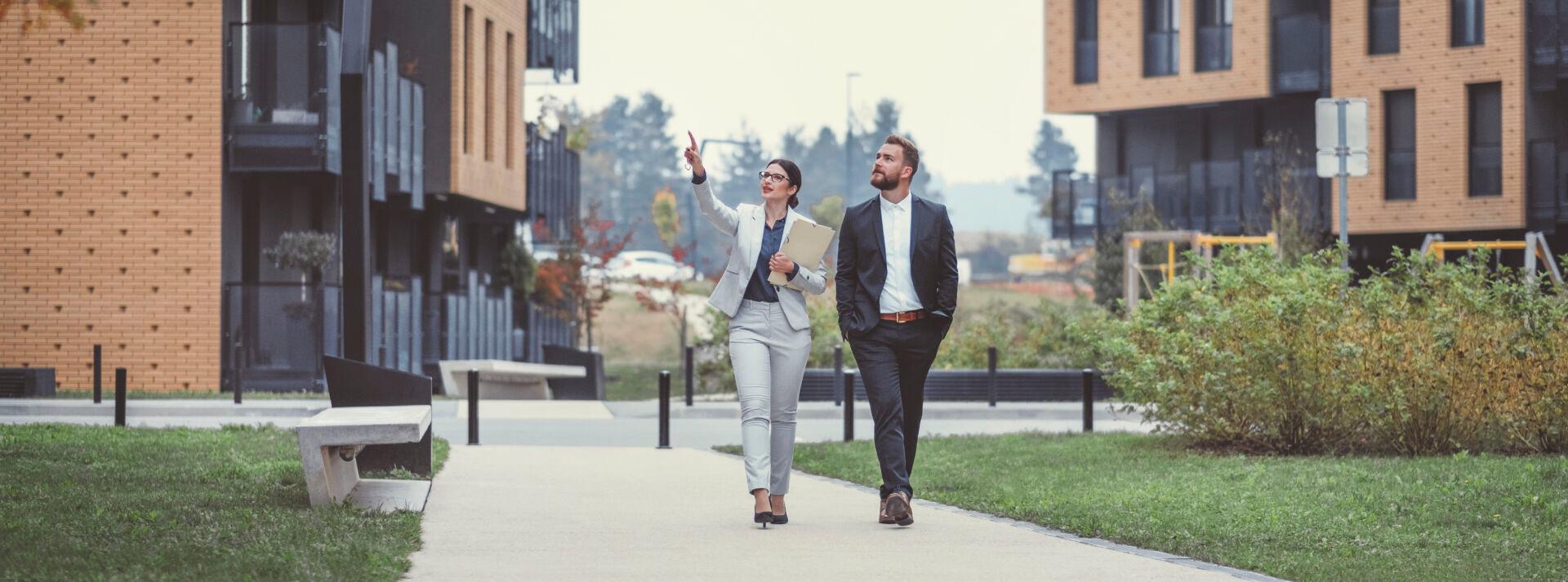 a man and a woman walking on sidewalk between two apartment buildings