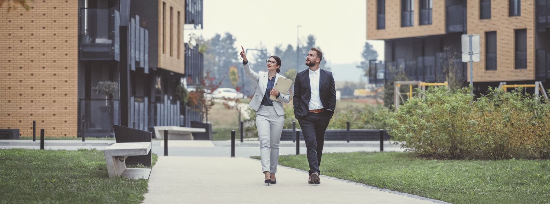 a man and a woman walking on sidewalk between two apartment buildings