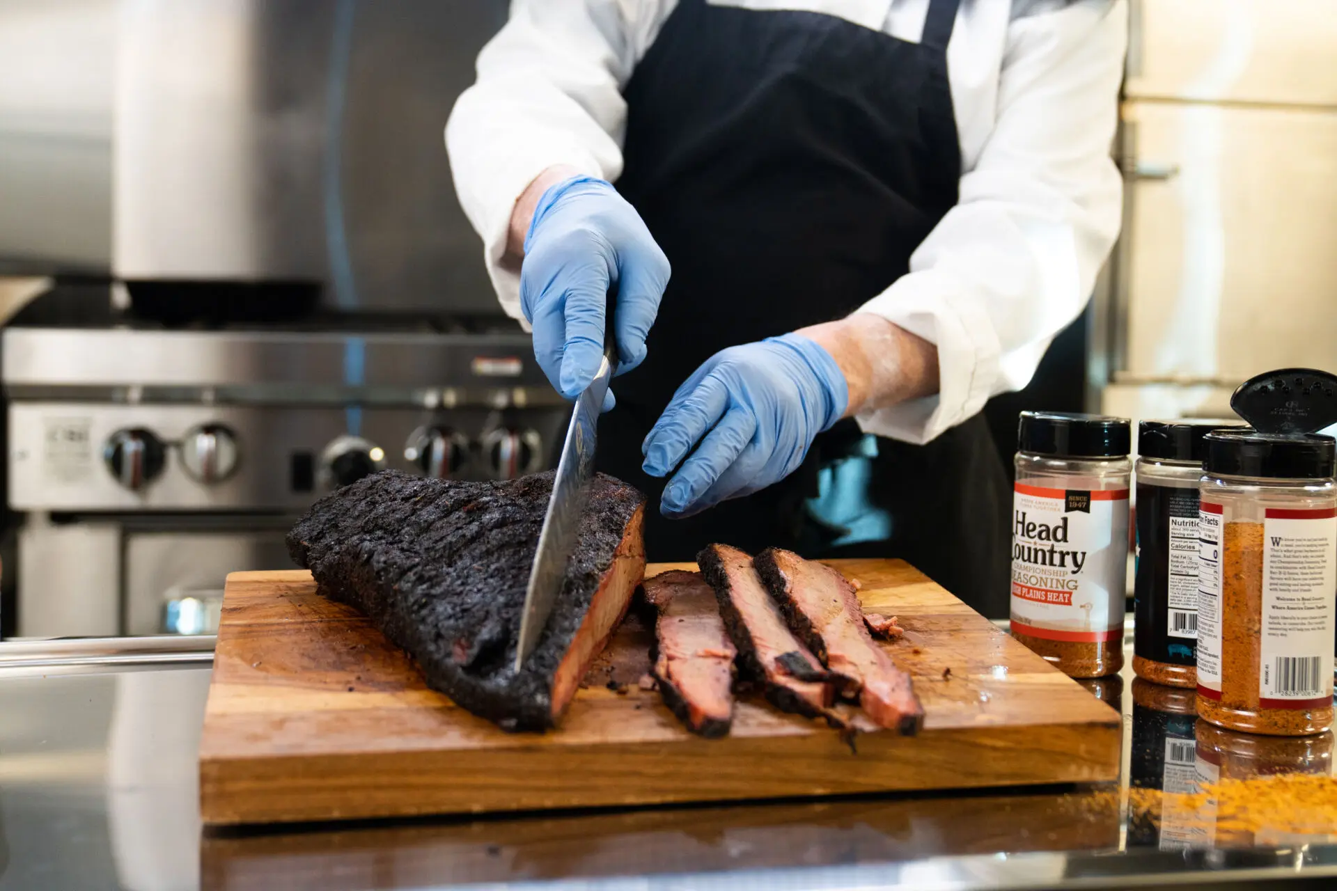 Chef slices spiced brisket on butcher block in OWS Foods test kitchen with