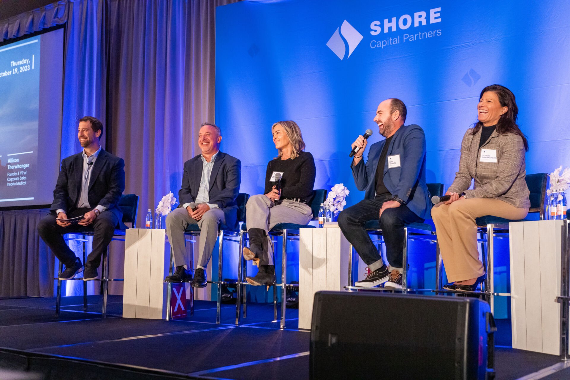 image of panel discussion on stage with laughing individuals seated on stools